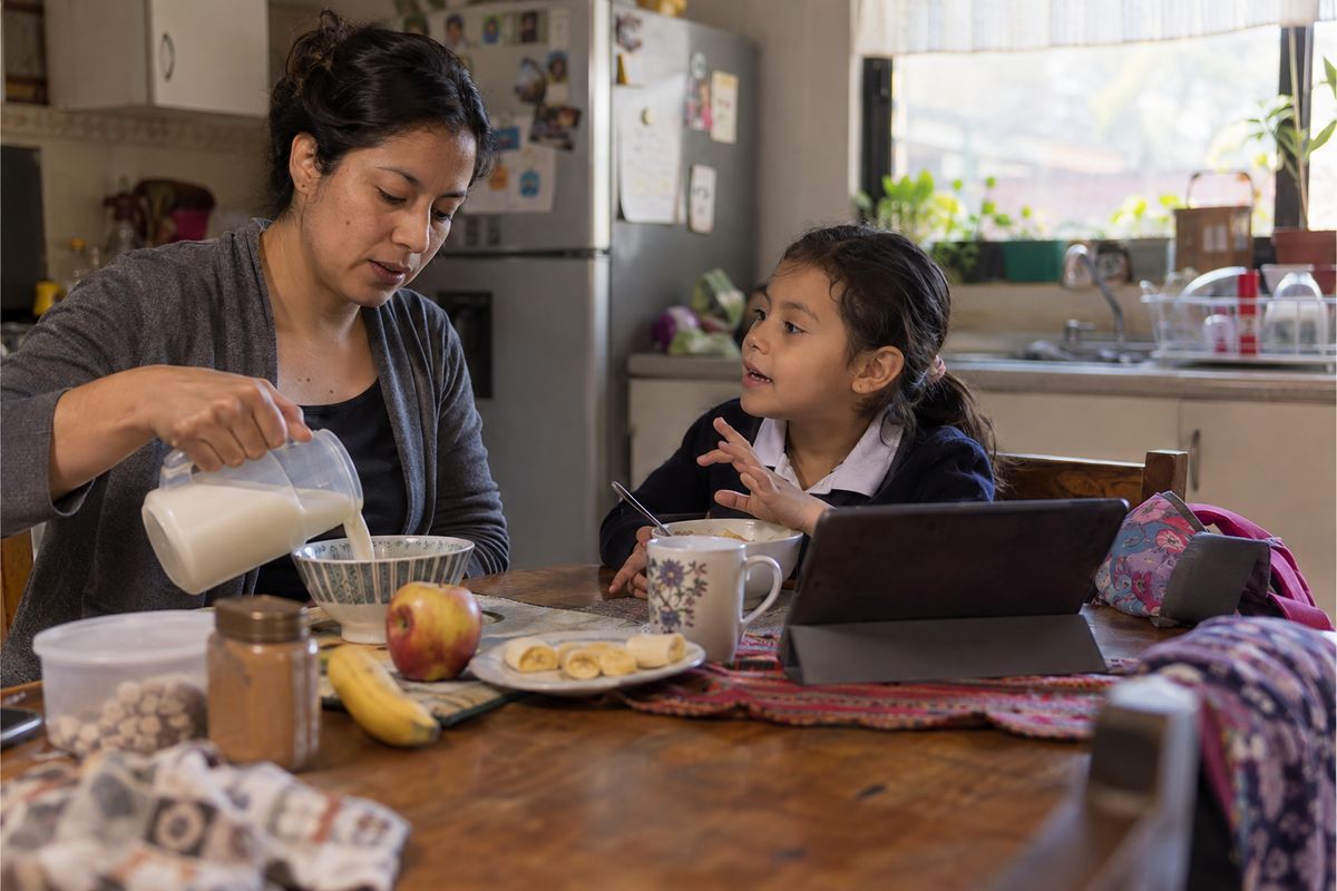 Una niña platicando con su mamá en el desayuno, con la historia abierta en la tablet